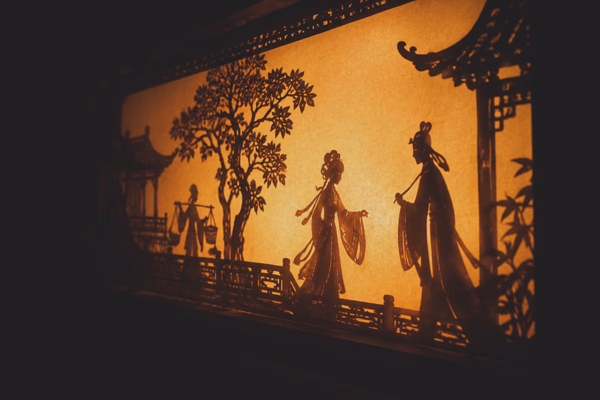 皮影戏台：暖橙色的灯光从纸幕后面透出，幕上是一组剪影人物与亭台树木